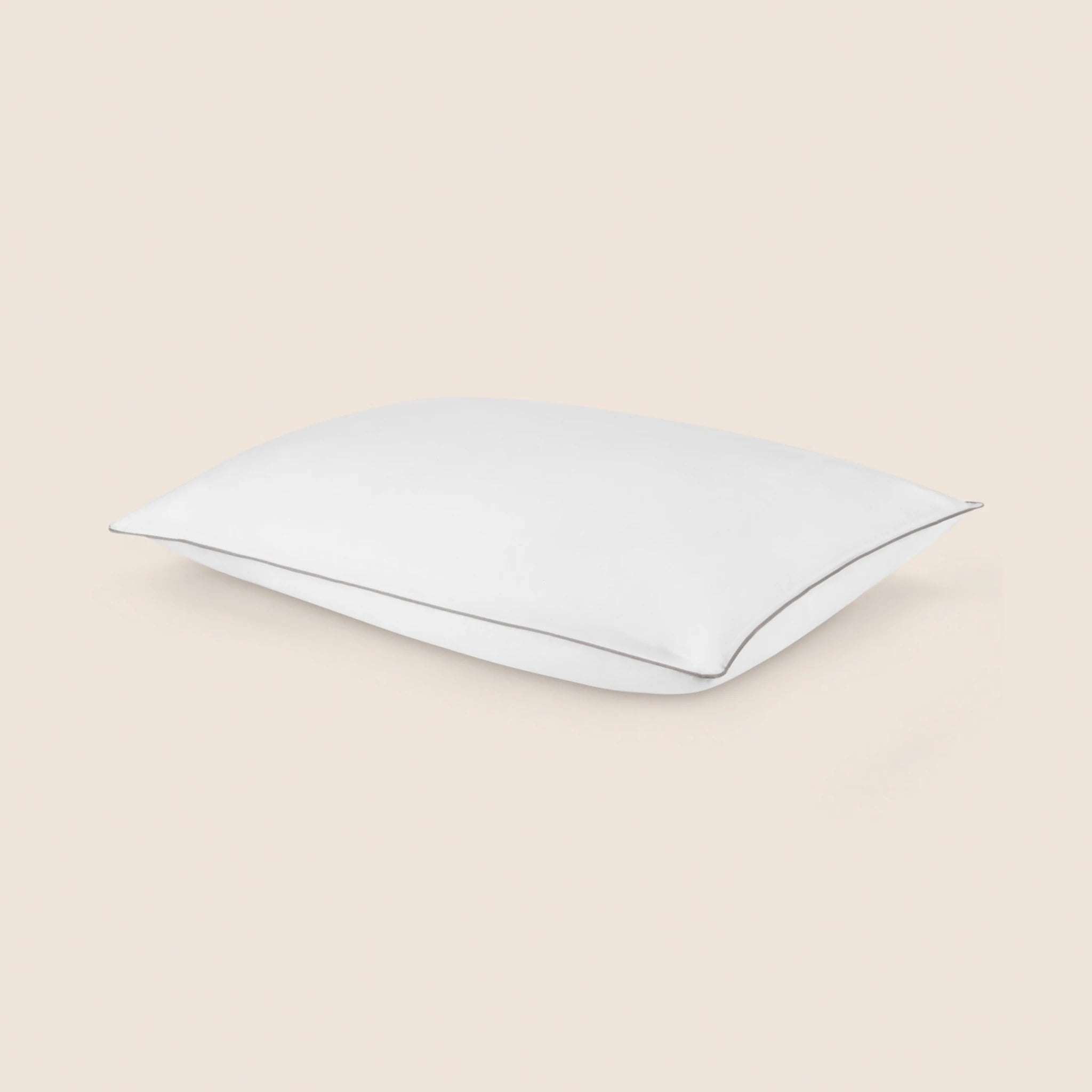 A white FluffCo-style hotel pillow with gray piping on a cream background